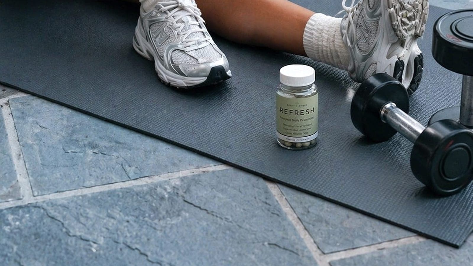 REFRESH bottle beside white trainers and workout gear on a cool mineral surface.